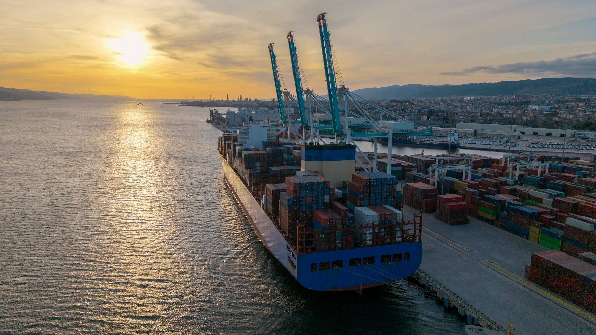 Container ship docked at a commercial port with cranes at sunset